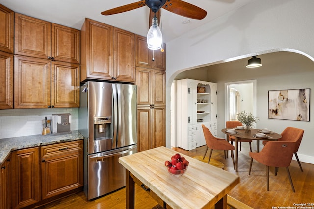 kitchen featuring stainless steel fridge with ice dispenser, brown cabinets, a ceiling fan, and arched walkways