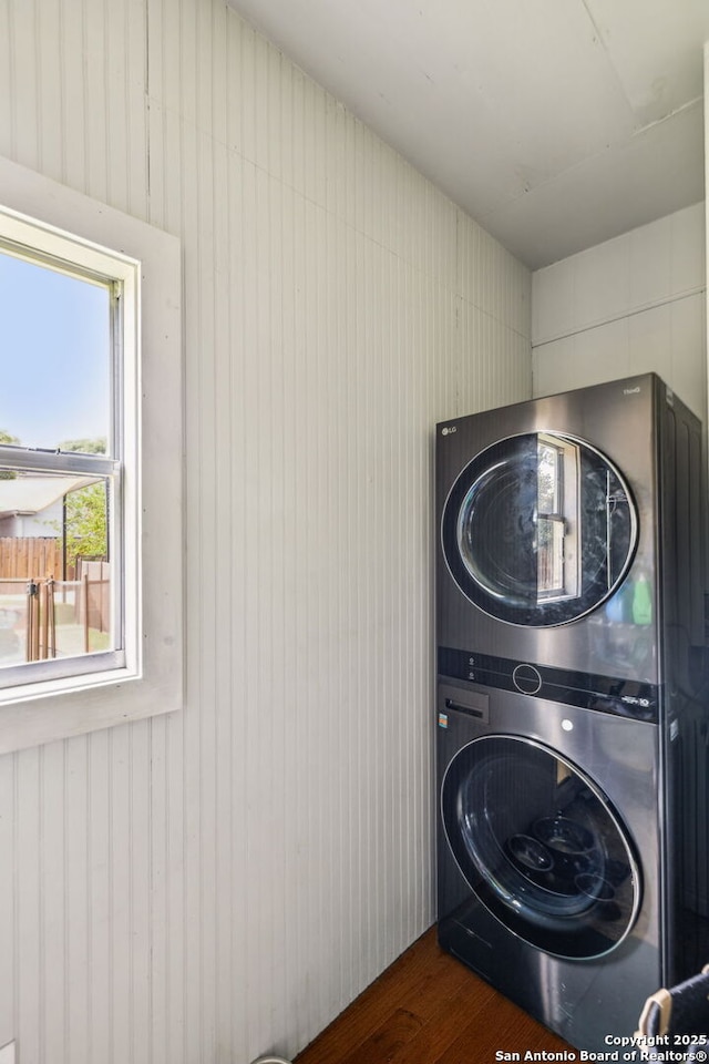 laundry room featuring stacked washer and clothes dryer, wood finished floors, and laundry area