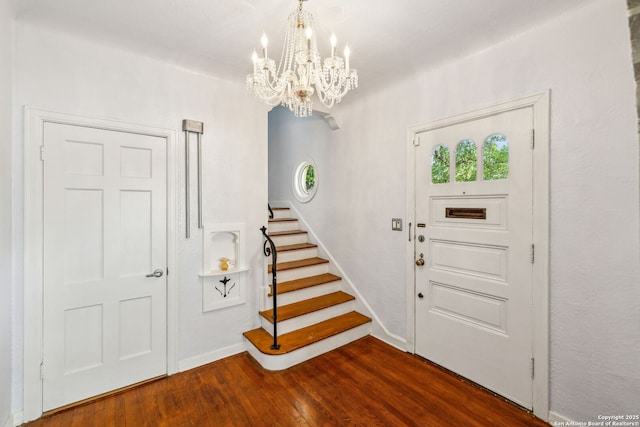 foyer featuring baseboards, a notable chandelier, dark wood finished floors, and stairway