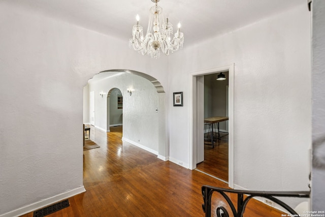 unfurnished dining area featuring an inviting chandelier, arched walkways, baseboards, wood finished floors, and visible vents