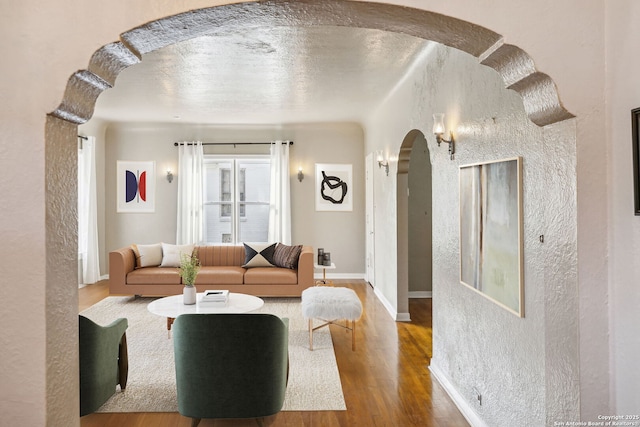 living area featuring baseboards, arched walkways, a textured wall, and wood finished floors