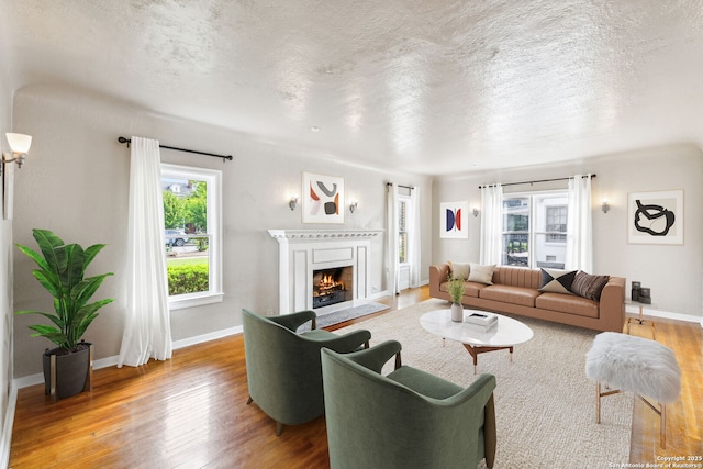 living room featuring baseboards, a textured ceiling, a warm lit fireplace, and wood finished floors