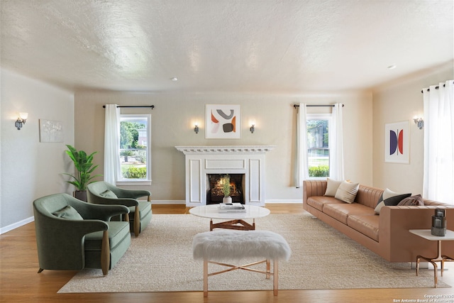living area featuring a textured ceiling, a warm lit fireplace, a healthy amount of sunlight, and wood finished floors