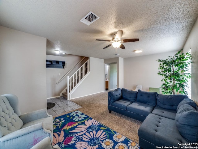 living area featuring ceiling fan, a textured ceiling, visible vents, carpet flooring, and stairs