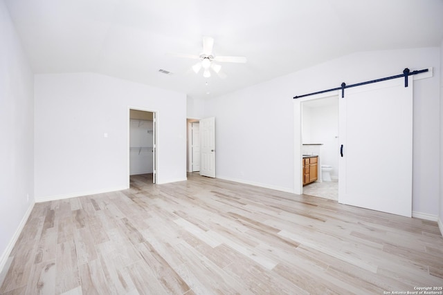 unfurnished bedroom with lofted ceiling, light wood finished floors, a barn door, and visible vents