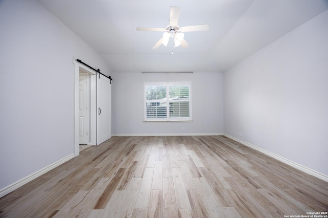 unfurnished bedroom featuring a ceiling fan, baseboards, a barn door, and light wood finished floors