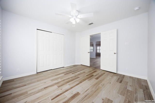 unfurnished bedroom featuring arched walkways, baseboards, light wood-type flooring, visible vents, and a closet