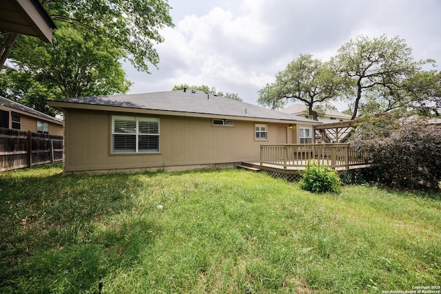 back of house featuring fence, a wooden deck, and a lawn