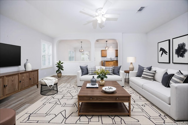 living area with a ceiling fan, visible vents, arched walkways, baseboards, and light wood-style flooring