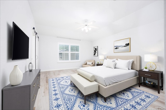 bedroom with ceiling fan, a barn door, baseboards, and light wood finished floors