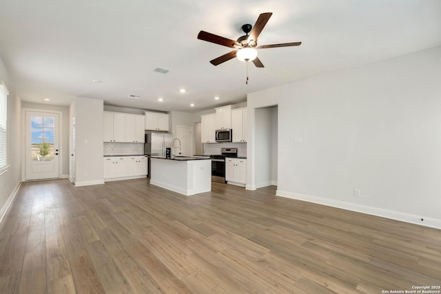 unfurnished living room featuring a sink, light wood-style floors, a ceiling fan, baseboards, and recessed lighting