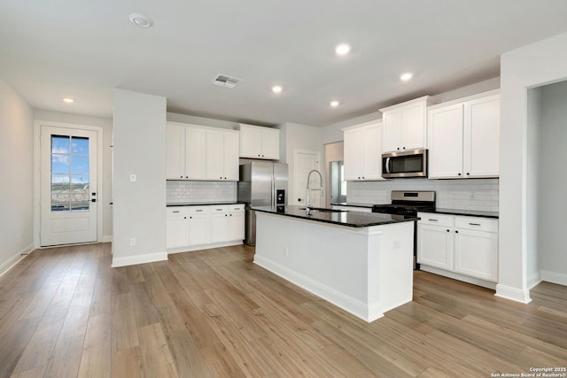kitchen with decorative backsplash, visible vents, appliances with stainless steel finishes, dark countertops, and a sink