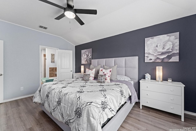 bedroom featuring visible vents, wood finished floors, baseboards, ensuite bath, and vaulted ceiling