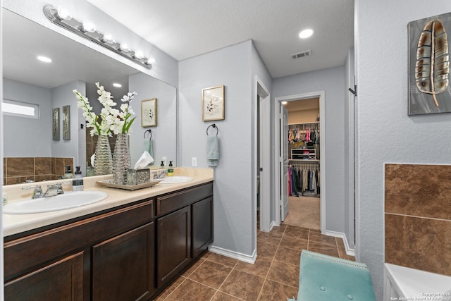 bathroom featuring double vanity, a walk in closet, visible vents, and a sink