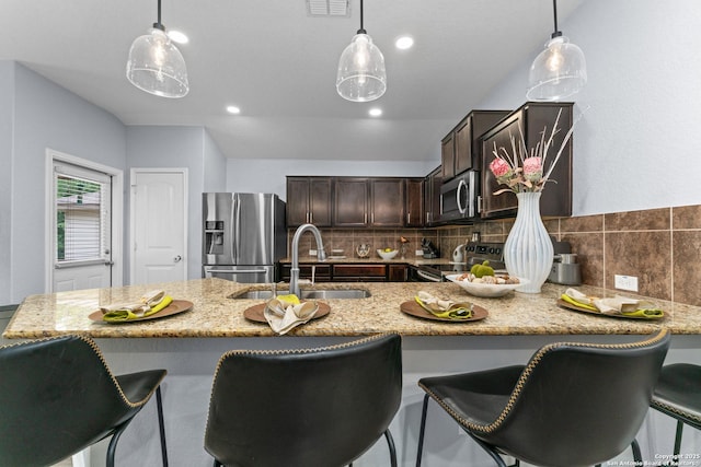 kitchen with dark brown cabinetry, light stone counters, a sink, stainless steel appliances, and backsplash