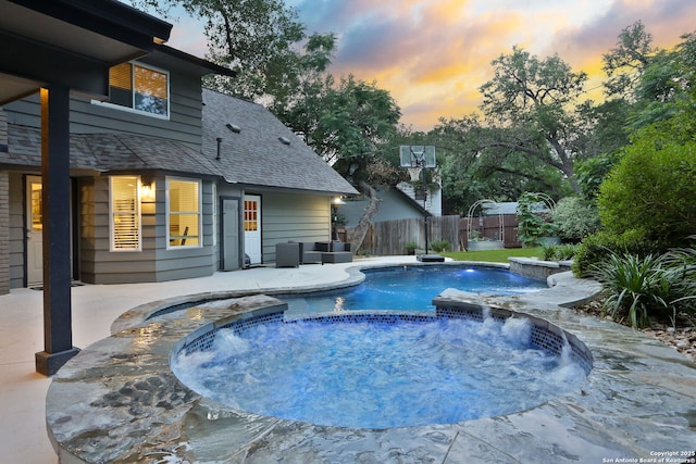 pool at dusk with a pool with connected hot tub, fence, and a patio area