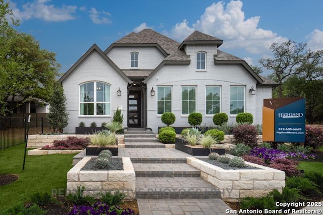 view of front of house with brick siding, fence, a shingled roof, and a front yard
