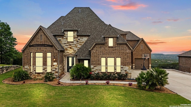 french country home with brick siding, a front yard, stone siding, and concrete driveway