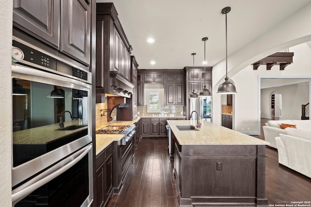 kitchen featuring a sink, arched walkways, stainless steel double oven, and dark brown cabinets