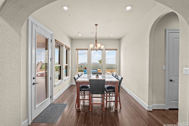 dining room featuring arched walkways, a textured wall, an inviting chandelier, and dark wood-style floors