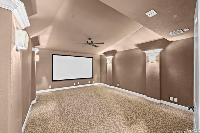 home theater with ceiling fan, a textured wall, visible vents, baseboards, and vaulted ceiling