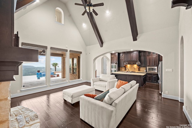 living area with ceiling fan, arched walkways, dark wood finished floors, baseboards, and high vaulted ceiling