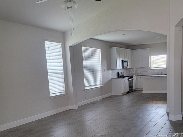 interior space featuring baseboards, arched walkways, dark wood finished floors, and ceiling fan
