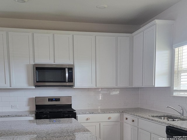 kitchen with a sink, white cabinets, light stone countertops, and stainless steel appliances