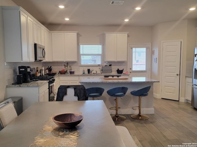 kitchen with light wood finished floors, stainless steel appliances, white cabinetry, decorative backsplash, and a kitchen bar