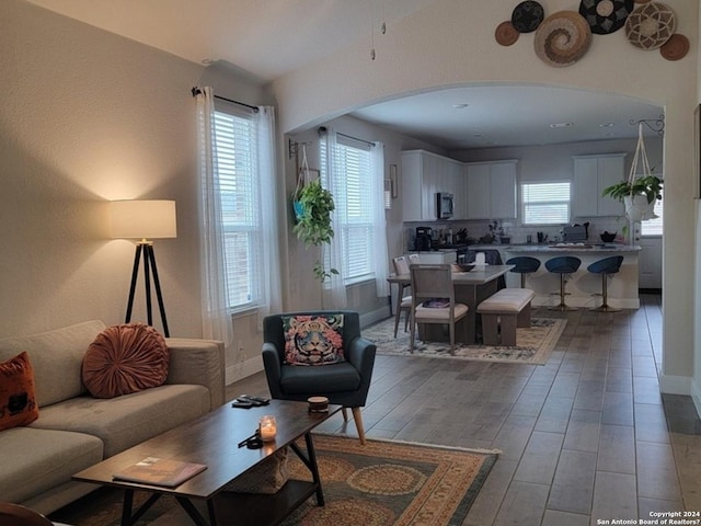 living room featuring arched walkways, baseboards, and light wood finished floors