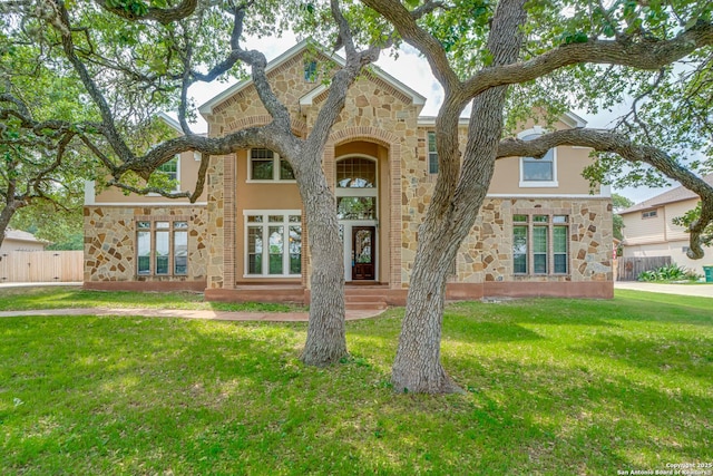 view of front of home featuring a front yard, fence, stone siding, and stucco siding