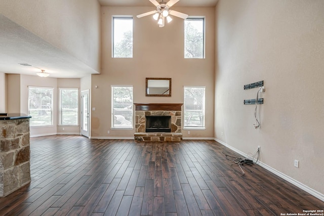 unfurnished living room with a fireplace, dark wood finished floors, a ceiling fan, baseboards, and a towering ceiling