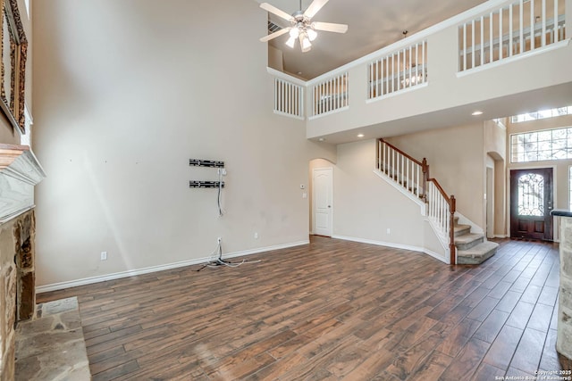 unfurnished living room with stairs, arched walkways, a high ceiling, and wood finished floors