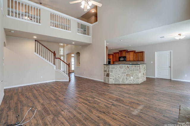 unfurnished living room with a towering ceiling, baseboards, arched walkways, a ceiling fan, and dark wood finished floors