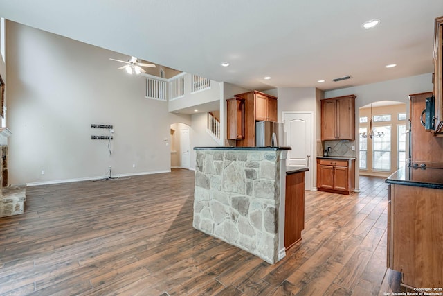kitchen with ceiling fan, backsplash, dark countertops, arched walkways, and wood finished floors