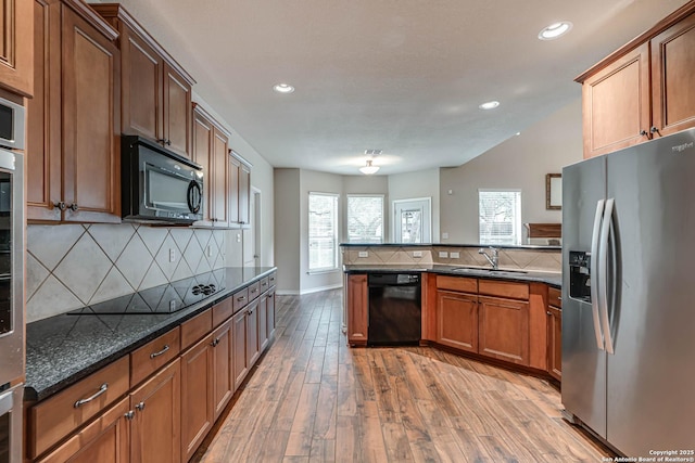 kitchen featuring decorative backsplash, a sink, black appliances, light wood finished floors, and a peninsula
