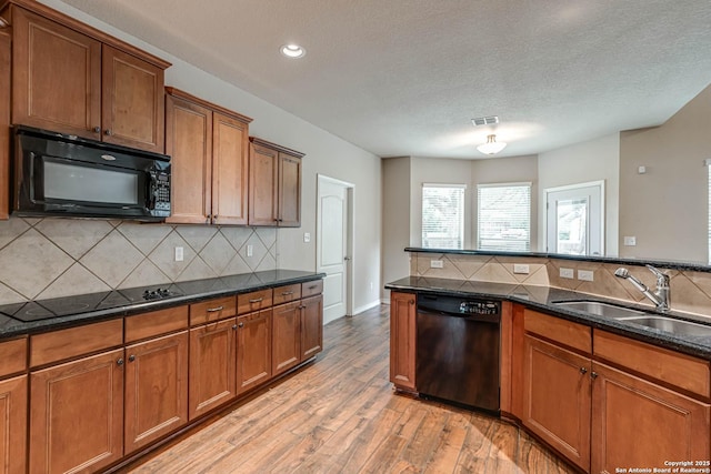 kitchen with brown cabinets, a sink, light wood-style flooring, backsplash, and black appliances