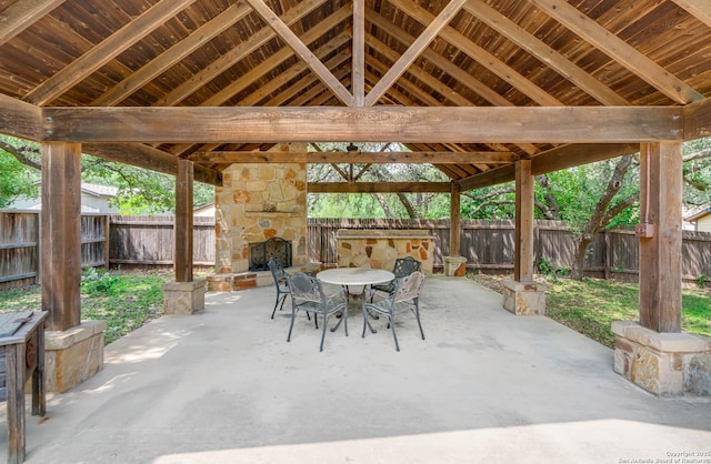 view of patio / terrace with an outdoor stone fireplace, a fenced backyard, outdoor dining space, and a gazebo