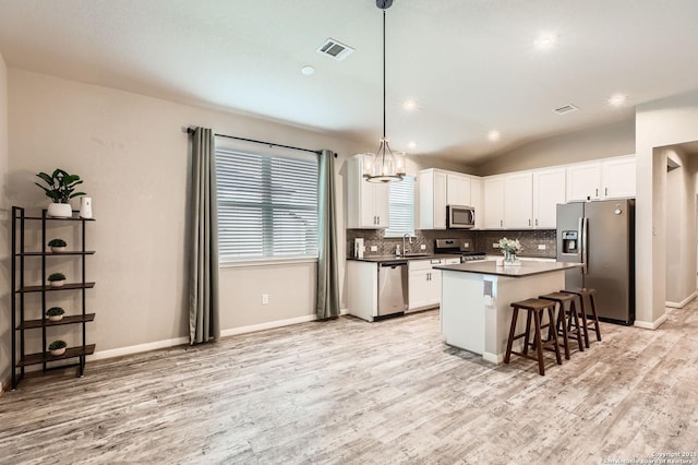 kitchen with a breakfast bar, stainless steel appliances, white cabinetry, decorative backsplash, and light wood-type flooring