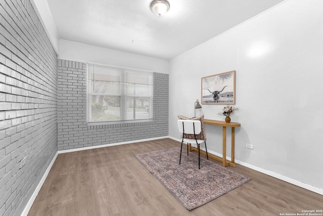 home office featuring brick wall, baseboards, and wood finished floors