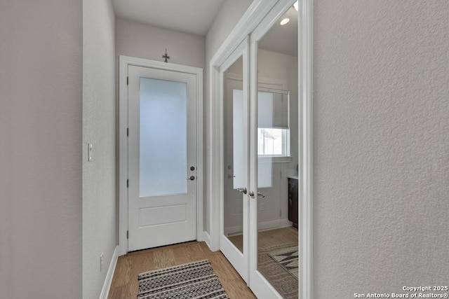 entryway with a textured wall, baseboards, and light wood finished floors