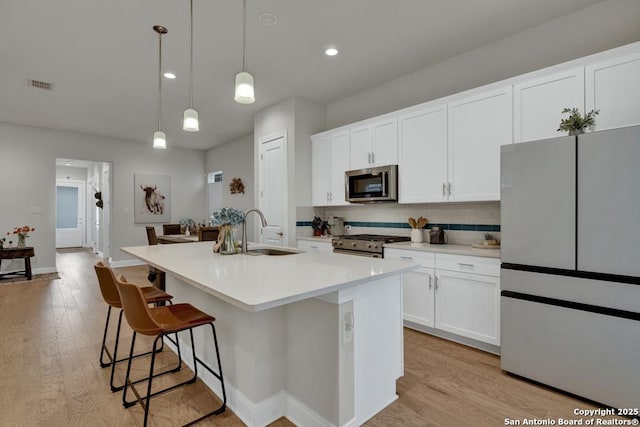 kitchen featuring visible vents, a kitchen island with sink, tasteful backsplash, a sink, and stainless steel appliances