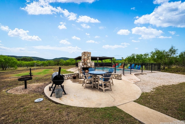 view of patio featuring an outdoor stone fireplace, a mountain view, fence, and a fenced in pool