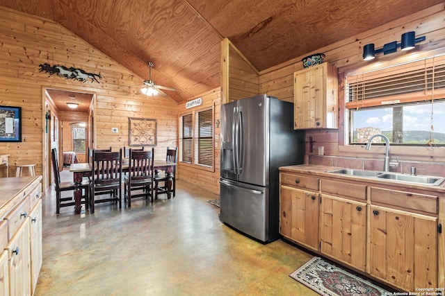 kitchen with vaulted ceiling, wood walls, a sink, concrete floors, and stainless steel fridge