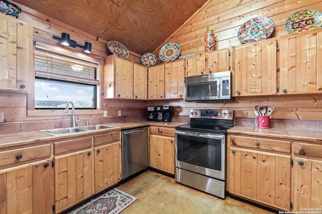 kitchen with a sink, tile counters, wood walls, stainless steel appliances, and vaulted ceiling