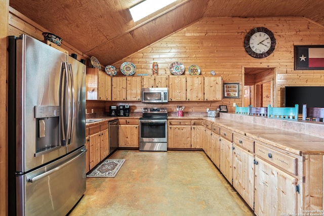 kitchen with a peninsula, light brown cabinetry, concrete flooring, vaulted ceiling with skylight, and appliances with stainless steel finishes