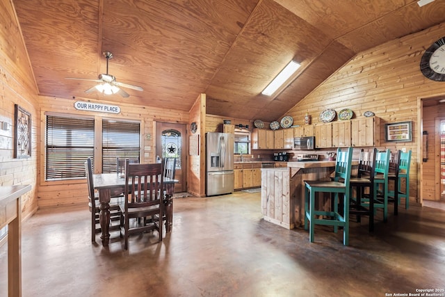 kitchen with wooden walls, ceiling fan, appliances with stainless steel finishes, concrete floors, and vaulted ceiling