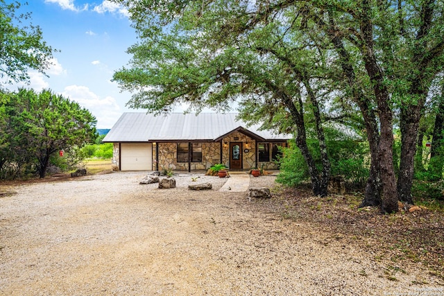 chalet / cabin featuring a porch, metal roof, dirt driveway, an attached garage, and stone siding