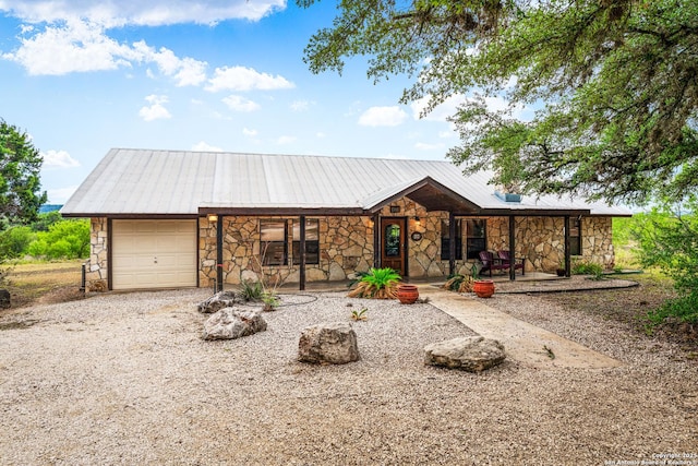 view of front of property featuring metal roof, stone siding, a garage, covered porch, and gravel driveway