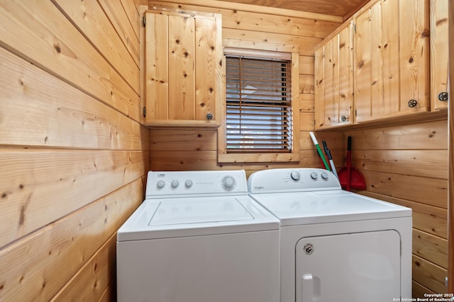 laundry area featuring cabinet space, wood walls, and washer and clothes dryer